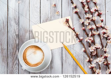 A cup of coffee next to the spring white flowers on wooden texture. Space for text.