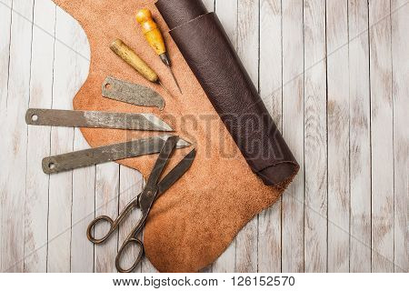 Leathersmith work desk . Pieces of hide and leather working tools on a work table.