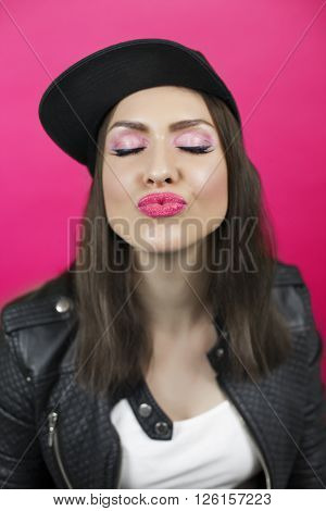 Beautiful young woman with closed eyes sends a kiss. Lips in focus. Black snapback cap and leather jacket. Pink background
** Note: Soft Focus at 100%, best at smaller sizes