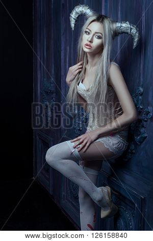 Beautiful blonde woman with horns on his head standing against the wall in the room.