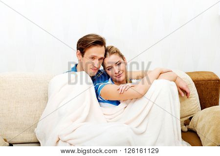 Smiling loving couple sitting on couch with blanket