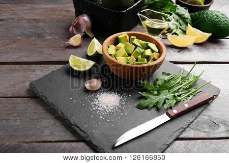 Diced avocado in wooden bowl with lime, garlic and arugula on slate plate