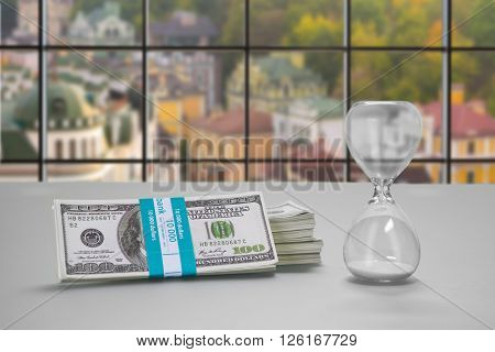 Desk with hourglass and dollars. Bundle of cash and hourglass. Clerk's table at daytime. Real estate at low prices.