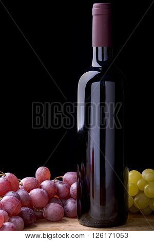 bottle of red wine with bunches of white and red grapes on wooden table
