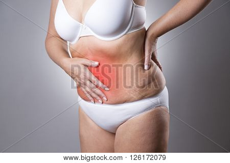 Woman in a white bra and white panties with abdominal pain on a gray background. Studio shot with red dot