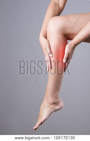 Pain in the calf muscle of the woman. Massage of female feet. Pain in the human body on a gray background with red dot