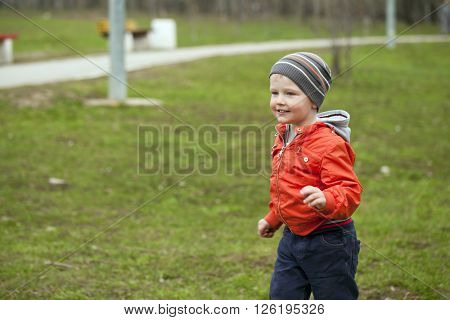 Close up portrait of a beautiful baby boy walking in spring park. Little boy in orange jaket and blue jeans, outdoors