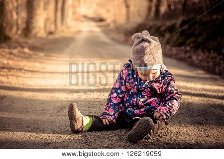 Little baby toddler sitting and playing on dirt road in winter evening