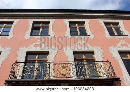 Building facade windows ornamented with frescoes and balcony. Red building facade windows rows decorated with classic paintings. Hand crafted iron balcony with golden ornaments. Patterns of building decorations. Crafted details of old house.