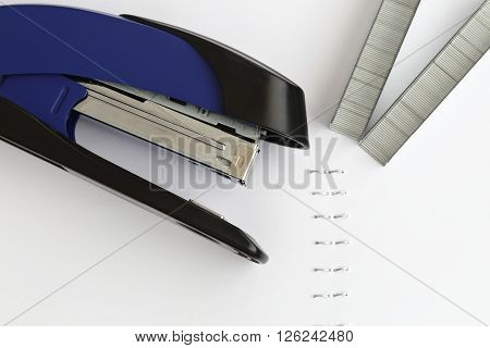 Blue stapler with staples and paper on the table selective focus