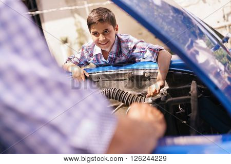 Family and Generation gap. Old grandpa spending time with his grandson. The senior man teaches to the preteen child to fix the engine of a vintage car from the 60s. They smile happy.