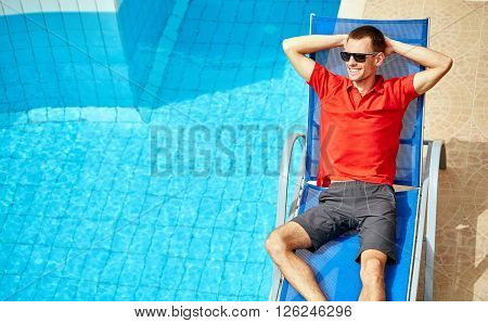 young man relaxing on the chaise-longue near the pool. man wearing in red polo shirt and sunglass
