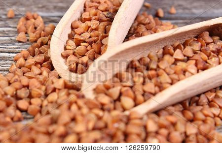 Heap of uncooked brown buckwheat groats with spoon on wooden table concept for healthy eating and nutrition