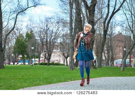 Young woman with leather bag walking in park among the trees