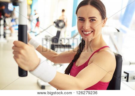 Young beautiful smiling woman is working out on butterfly machine at the gym