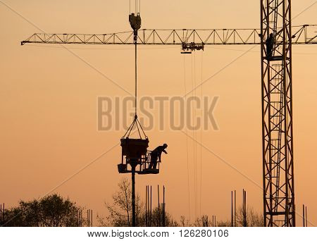 Silhouette of construction worker on the crane at sunset