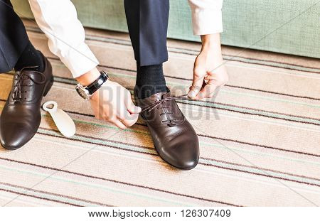 A young man tying elegant shoes indoors.