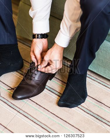 A young man tying elegant shoes indoors.