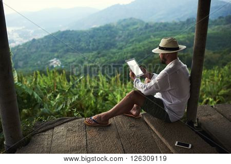 Male wanderer is holding portable touch pad with copy space on the screen for your text message or promotional content.Young man is reading financial news on digital tablet during his trip in Thailand