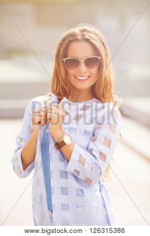 Attractive fashionable middle-aged woman standing in a street looking thoughtfully at the camera with a charming friendly smile. Toned image.