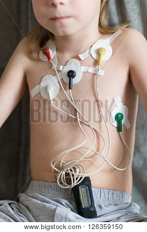 Child sitting on the sofa. Heart cardiogram or monitoring of cardiac performance using Holter.