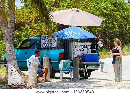 BIG PINE KEY, USA - MAY 10, 2015: Man selling icecold coconuts out of a pick-up truck in Veterans Memorial Park in Little Duck Key. A woman is standing in front of it considering buying a coconut.