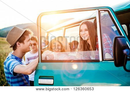 Group of teenage hipsters on a roadtrip having fun, standing at the campervan. Young friends outside on a summer day.
