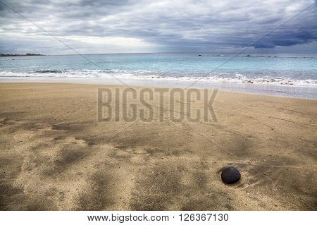 A beach coloured with gold sand and a small rock over it
