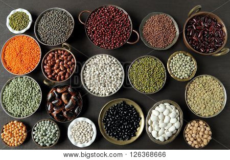 Beans peas and lentils in metal bowls on dark background.