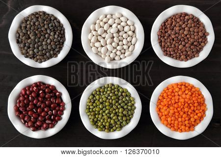 Colorful beans and lentils in ceramic bowls on a dark background.