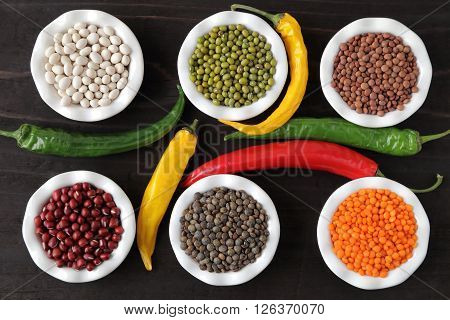 Colorful beans and lentils in ceramic bowls on a dark background.