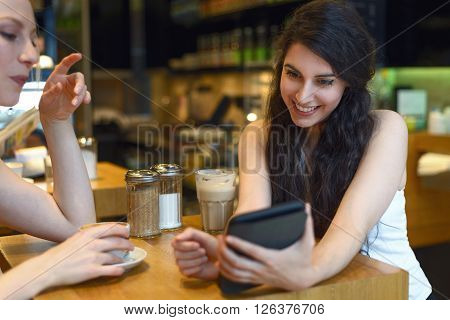Two young women looking at a digital tablet as they sit enjoying coffee together in a bistro or coffeebar