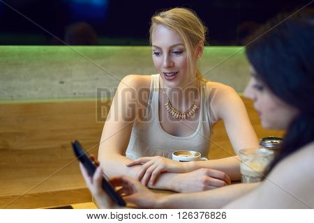 Two young women looking at a digital tablet as they sit enjoying coffee together in a bistro or coffeebar