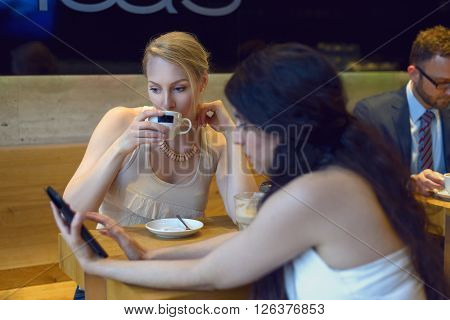 Two young women looking at a digital tablet as they sit enjoying coffee together in a bistro or coffeebar