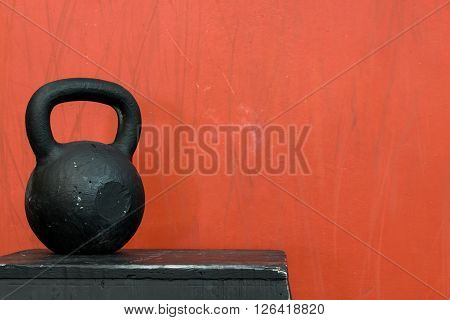 Black kettle bell on a black jump box, against a red wall