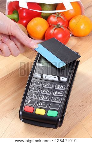 Using credit card reader payment terminal with contactless credit card and  fruits and vegetables in paper shopping bag cashless paying for shopping
