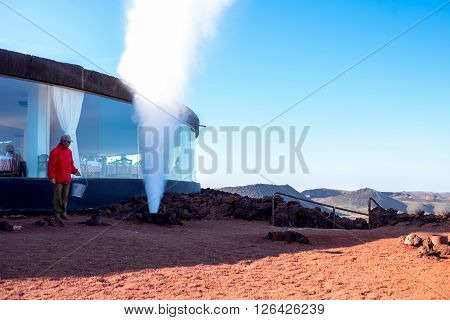 TIMANFAYA PARK, LANZAROTE ISLAND, SPAIN - SIRCA JANUARY 2016: Man shows natural geyser for tourists in Timanfaya park. This park is entirely made up of volcanic soil and was designed by Cesar Manrique