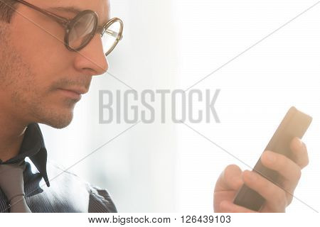 Businessman with eyeglasses typing messages on his smartphone.