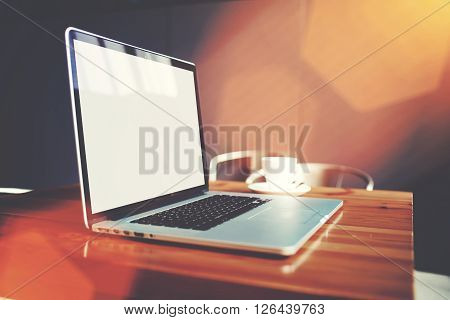 Open laptop computer and cup of coffee lying on wooden table in cafe bar interior portable net-book and mug of cappuccino remote job via internet freelance work filtered image with flare sun light