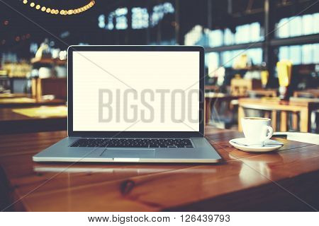 Open laptop computer and cup of coffee lying on a wooden table in cafe bar interior portable net-book with copy space screen for your information content or text message freelance work via internet