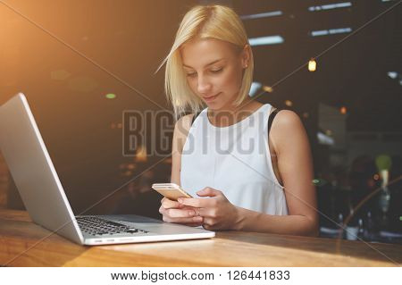 Beautiful lady chatting on smart phone while sitting at the table with laptop computer in cafe bar interior pretty European woman using cell telephone while relaxing after work on portable net-book