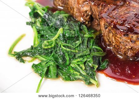 Delicious grilled fillet mignon steak with chard covered with red wine sauce. Macro. Selective focus on heap of chard. Photo can be used as a whole background.