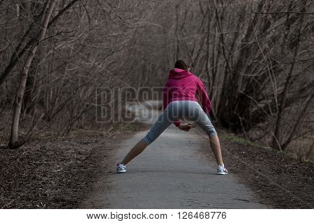 Beautiful young woman doing stretching exercises before running in the park