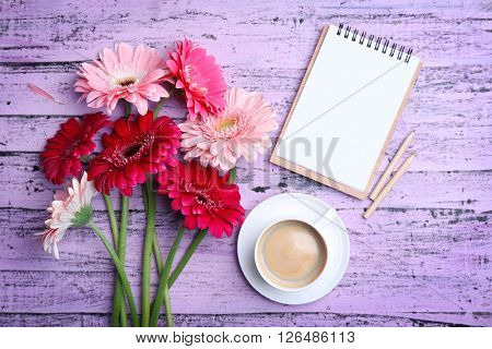 Gerbers and cup of coffee on wooden purple background
