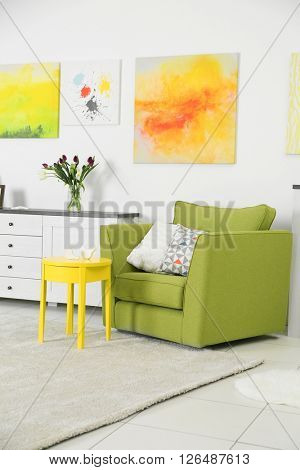 Modern living room interior with green chair, yellow coffee table and bright canvases on the white wall