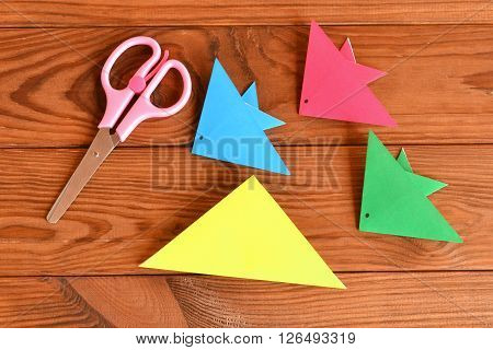 Paper sheets, scissors on a brown wooden table. How to make origami fish