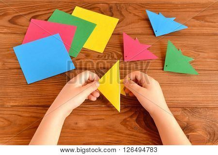 Origami colorful fish, paper sheets. Child holds an yellow origami fish in his hands. Brown wooden background