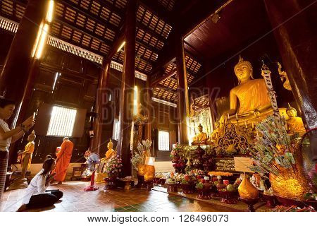 CHIANG MAI, THAILAND - FEB 22: People praying inside sunny hall of historical wooden temple with golden Buddha statue on February 22, 2016. King Mengrai founded the city of Chiang Mai in 1296