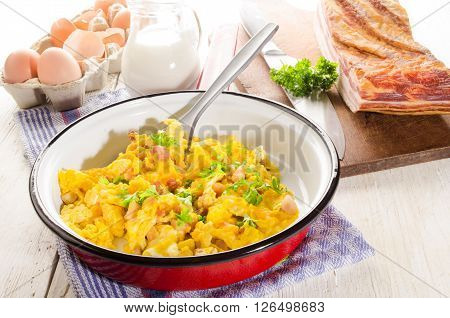 scrambled eggs with fat smooked bacon parsley and milk in a pan