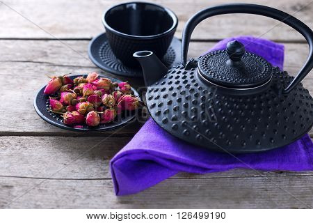 Dry rose tea in bowl and traditional asian tea set on aged wooden background. Selective focus is on tea. Toned image.